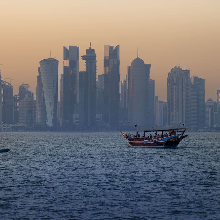 The Doha skyline at sunset behind a traditional dhow