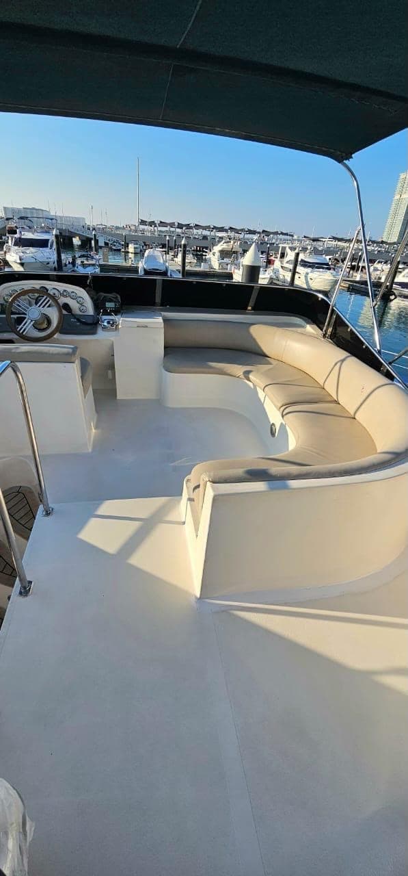 The yacht's shaded upper deck, with a curved bench seat and the helm, moored in a Dubai marina