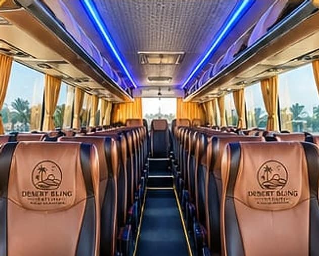 The coach cabin from the front, two rows of tan headrest covers running down each side of the aisle under blue ceiling lighting