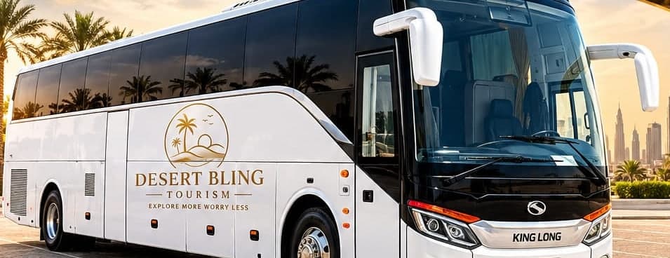 The 50-seat coach at sunset, three-quarter front view with the Desert Bling Tourism mark along its white flank and the Dubai skyline behind it