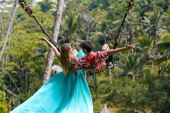 A couple on a jungle swing soaring out over the Bali treetops