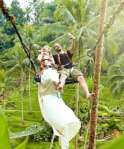 A couple taking a selfie on a Bali swing among the palms above the rice terraces