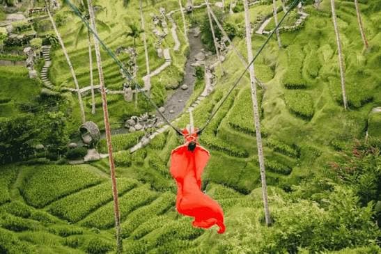 A rider in a flowing red dress on a Bali swing above the rice terraces